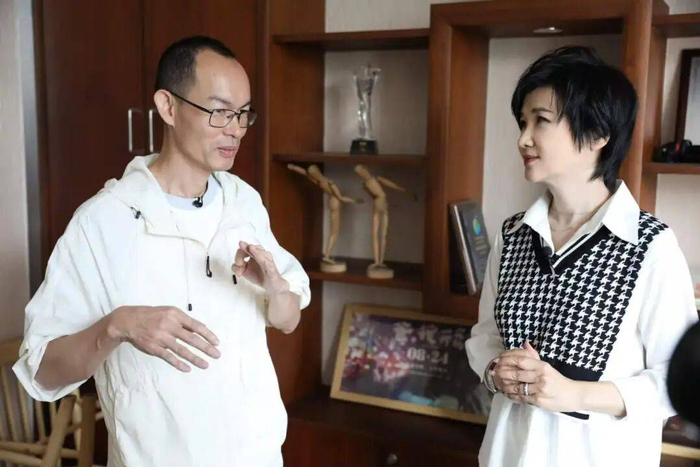 吴小莉参观蓝鸿春的办公室，他们身后的海报上是蓝鸿春执导的第一部潮汕电影《爸，我一定行的》
